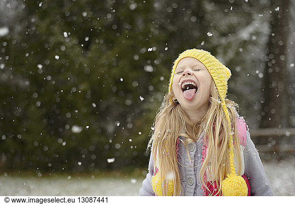 Playful girl sticking out tongue during snowfall