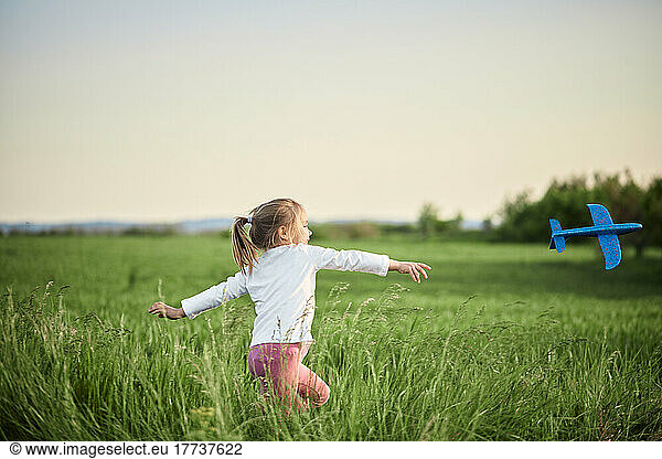 Playful girl throwing airplane in agricultural field