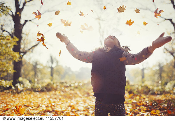 Playful girl throwing autumn leaves overhead in sunny park