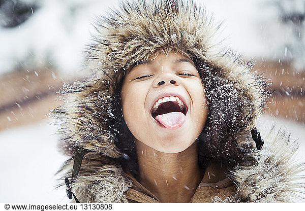 Playful girl with mouth open tasting snow during snowfall