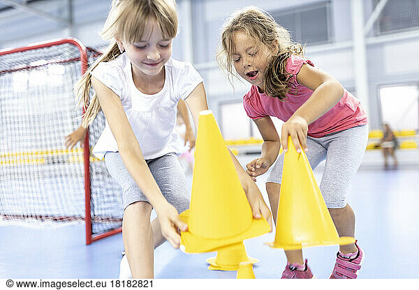Playful girls picking up cones at school sports court