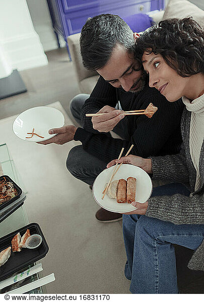 Playful husband feeding egg roll to wife with chopsticks