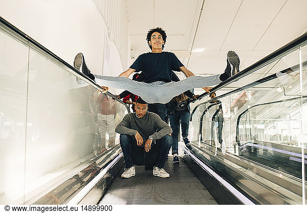 Playful male friends on moving walkway in shopping mall