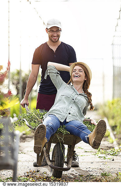 Playful man and woman having fun with a wheelbarrow in a greenhouse