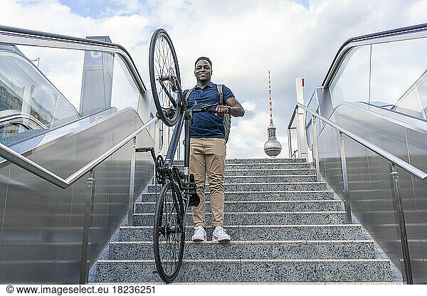 Playful man carrying bicycle moving down on staircase