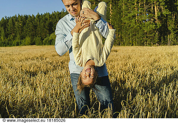Playful man carrying happy daughter upside down on field
