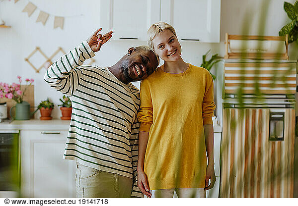 Playful man gesturing hand sign head cocked with girlfriend in kitchen