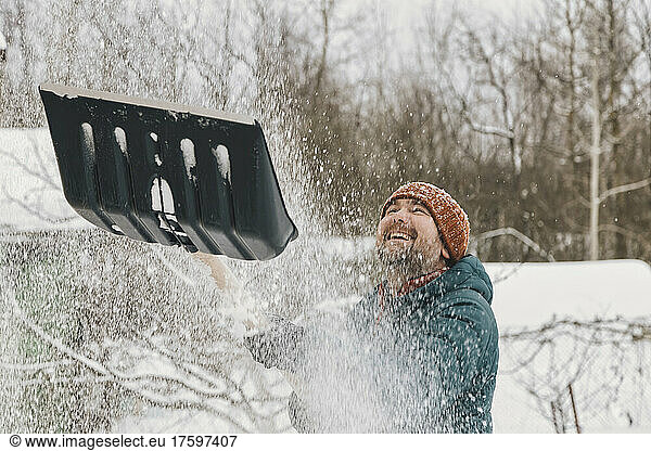 Playful man throwing snow from snow shovel in winter