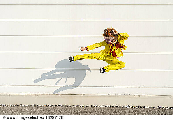 Playful man wearing animal mask jumping and kicking in front of wall