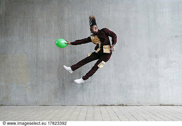 Playful man with balloon jumping in front of concrete wall