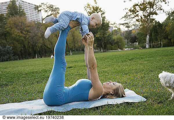 Playful mother and son doing yoga near dog in park