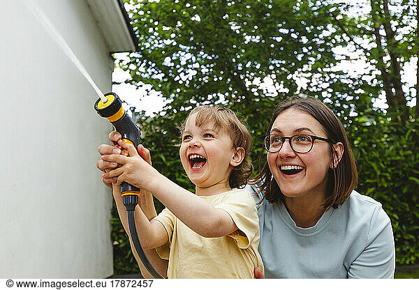 Playful mother and son spraying water through garden hose