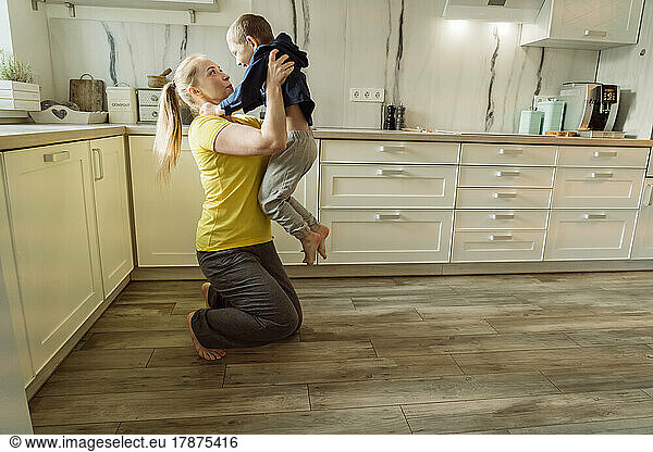 Playful mother carrying son in kitchen at home