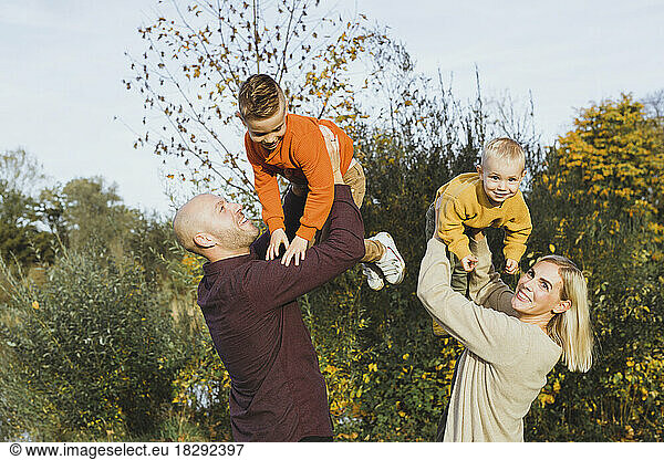 Playful parents lifting children in autumn