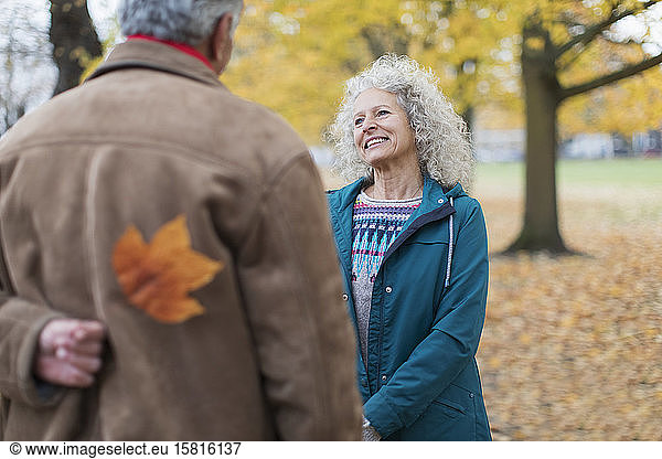 Playful senior husband surprising wife with autumn leaf in park