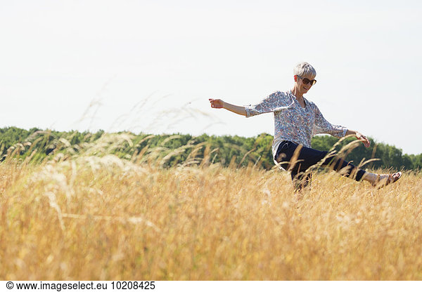 Playful senior woman dancing in sunny rural field