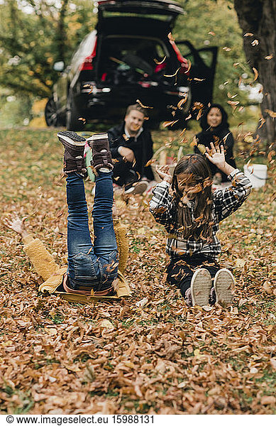Playful sisters enjoying on autumn leaves during picnic with parents