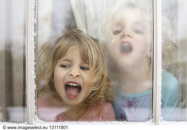 Playful sisters in house seen through window during winter