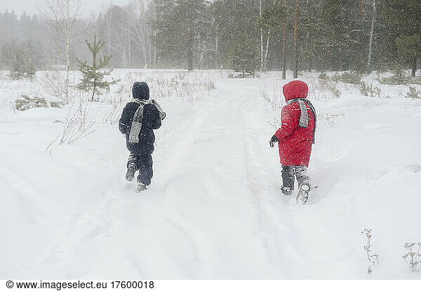 Playful twin brothers running in snow forest
