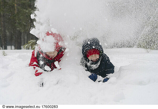 Playful twin brothers throwing snow on each other in forest
