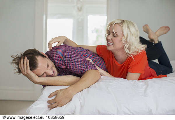 Playful wife tickling husband on bed