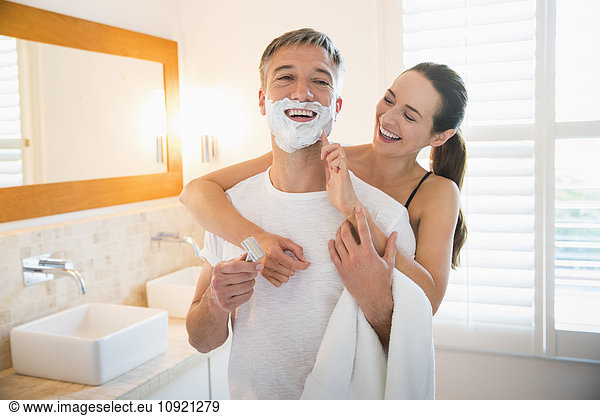 Playful wife wiping shaving cream on husband’s face in bathroom