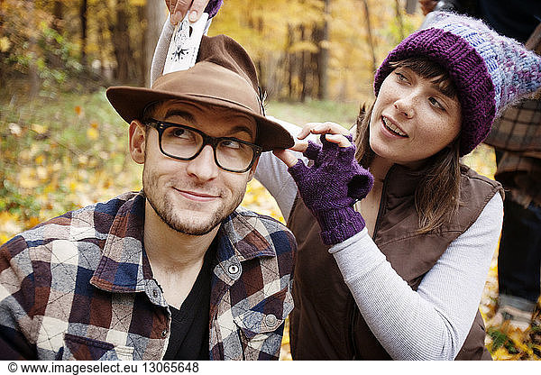 Playful woman putting card in man's hat at field