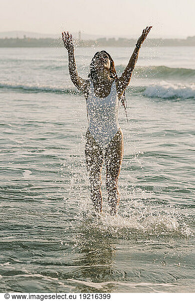 Playful woman splashing and standing in water at beach