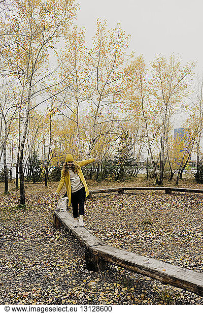 Playful woman walking on wooden benches at park during autumn