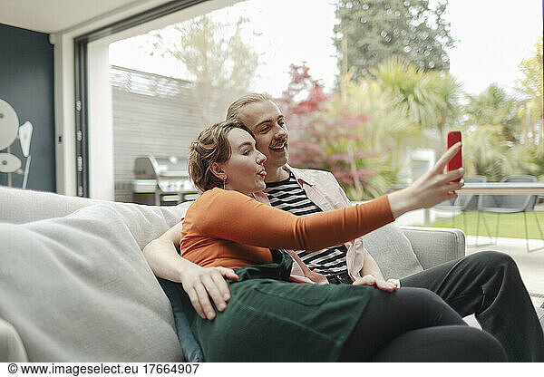 Playful young couple taking selfie with smart phone on sofa