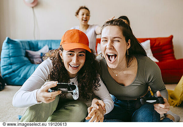 Playful young female friends playing video game at home
