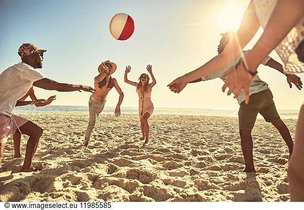 Playful young friends playing with beach ball on sunny summer beach