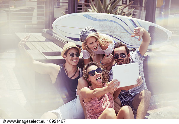 Playful young friends taking selfie in front of surfboard with digital tablet