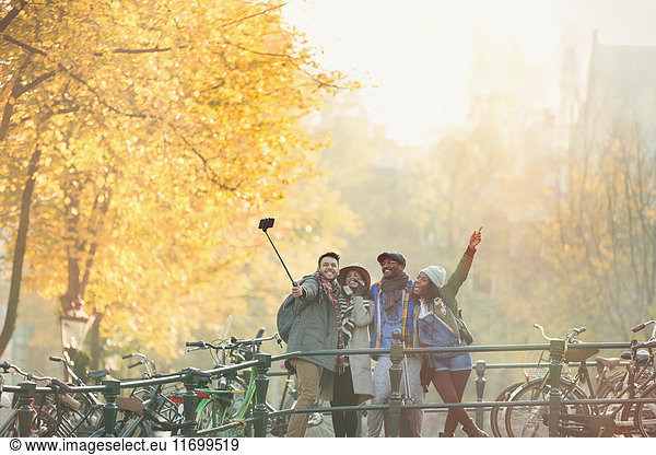 Playful young friends taking selfie with selfie stick on urban autumn bridge  Amsterdam
