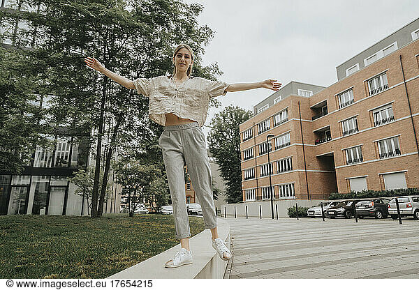 Playful young woman with arms outstretched balancing on wall