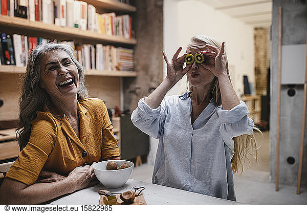 Playful young woman with mother covering her eyes with kiwis
