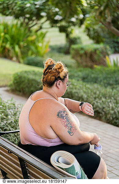 Plus sized woman portrait sitting on bench looking at smart watch