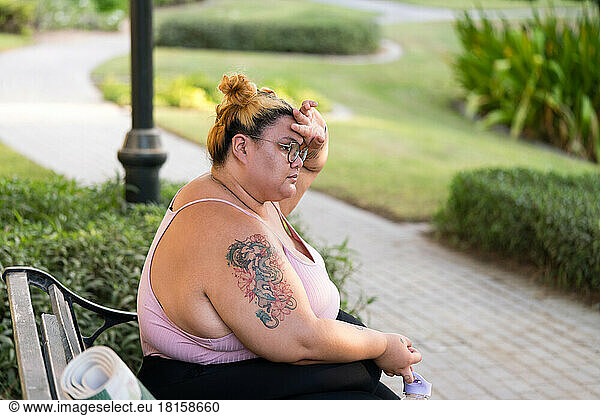 Plus sized woman portrait sitting on bench resting after workout
