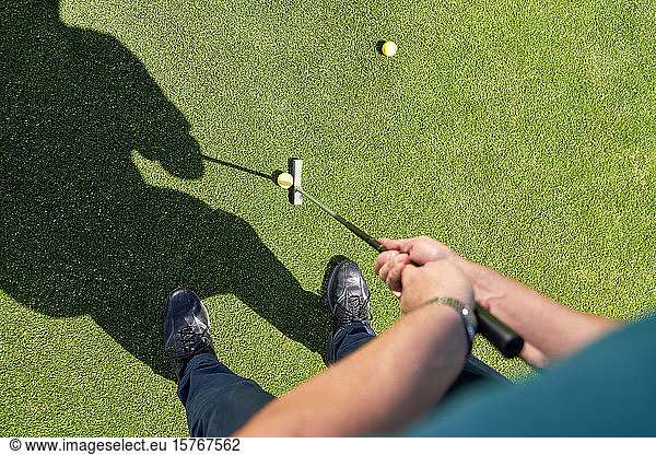 Point of view man putting golf ball on sunny greens