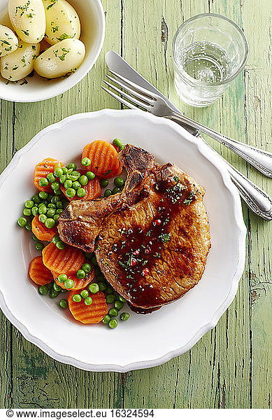 Pork chop with carrots  peas and boiled potatoes on plate