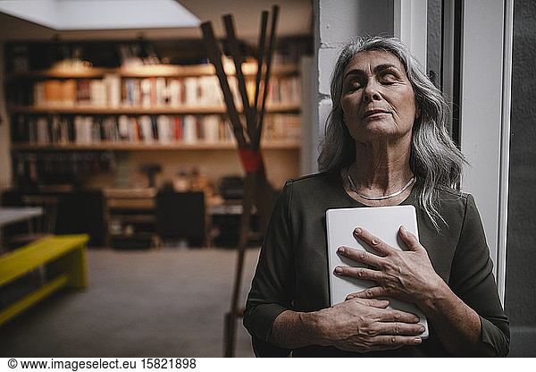 Portait of grey-haired businesswoman with closed eyes holding tablet in a loft office