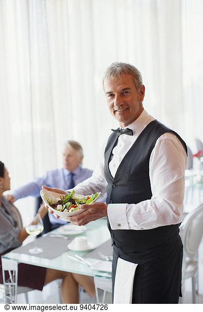 Porträt des Kellners mit Salatschüssel  Menschen am Tisch im Hintergrund