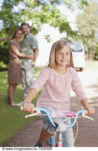 Porträt des lächelnden Mädchens auf dem Fahrrad mit Eltern im Hintergrund