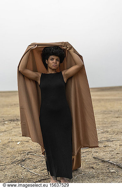 Porträt einer barfüssigen jungen Frau  die in trostloser Landschaft steht und eine Decke hält