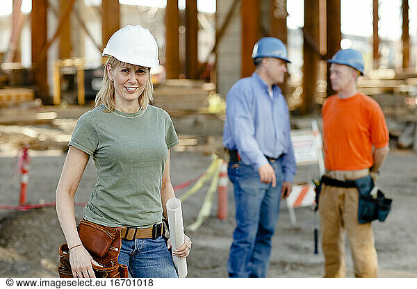 Porträt einer Bauarbeiterin mit zwei Arbeitern dahinter