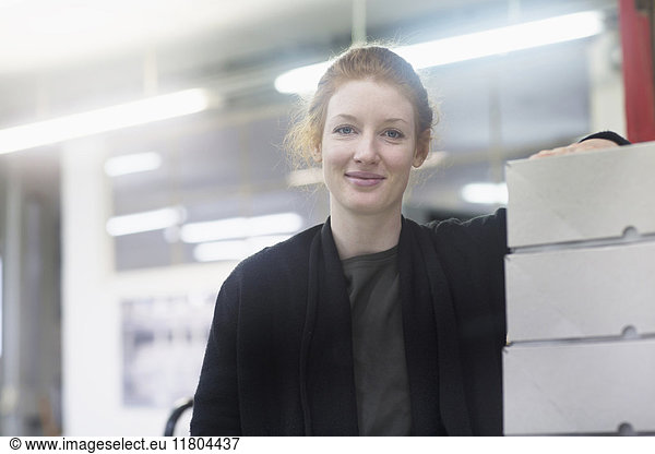 Porträt einer Frau mit einem Haufen Kisten in den Händen an einer Presse
