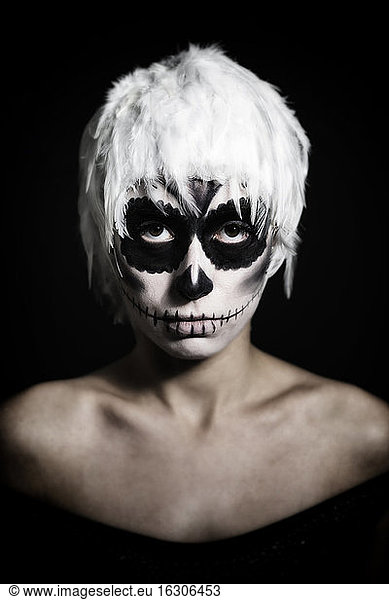 Porträt einer Frau mit Totenkopf-Make-up und Kopfbedeckung aus weißen Federn  Studioaufnahme