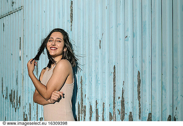 Porträt einer glücklichen brünetten jungen Frau  die an einer heruntergekommenen Wand steht