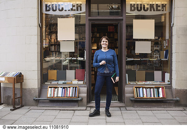 Porträt einer glücklichen Frau  die ein Buch hält  während sie vor der Buchhandlung steht.