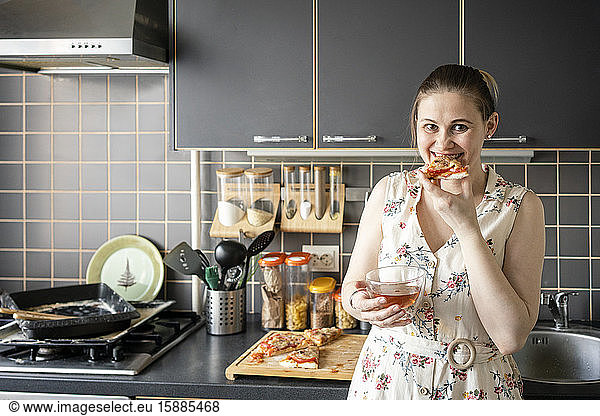 Porträt einer glücklichen Frau  die in der Küche hausgemachte Pizza isst